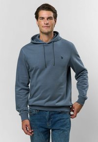 Svetlomodrá mikina s kapucňou a predným vreckom, s nastaviteľnou šnúrkou. Vyrobená z mäkkej tkaniny, s malým logom na hrudi. V kombinácii s modrými džínami.