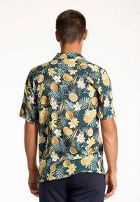 Camisa de manga corta en tejido verde oscuro, con un patrón floral y de cítricos en amarillo, blanco y toques de marrón, con un corte relajado.
