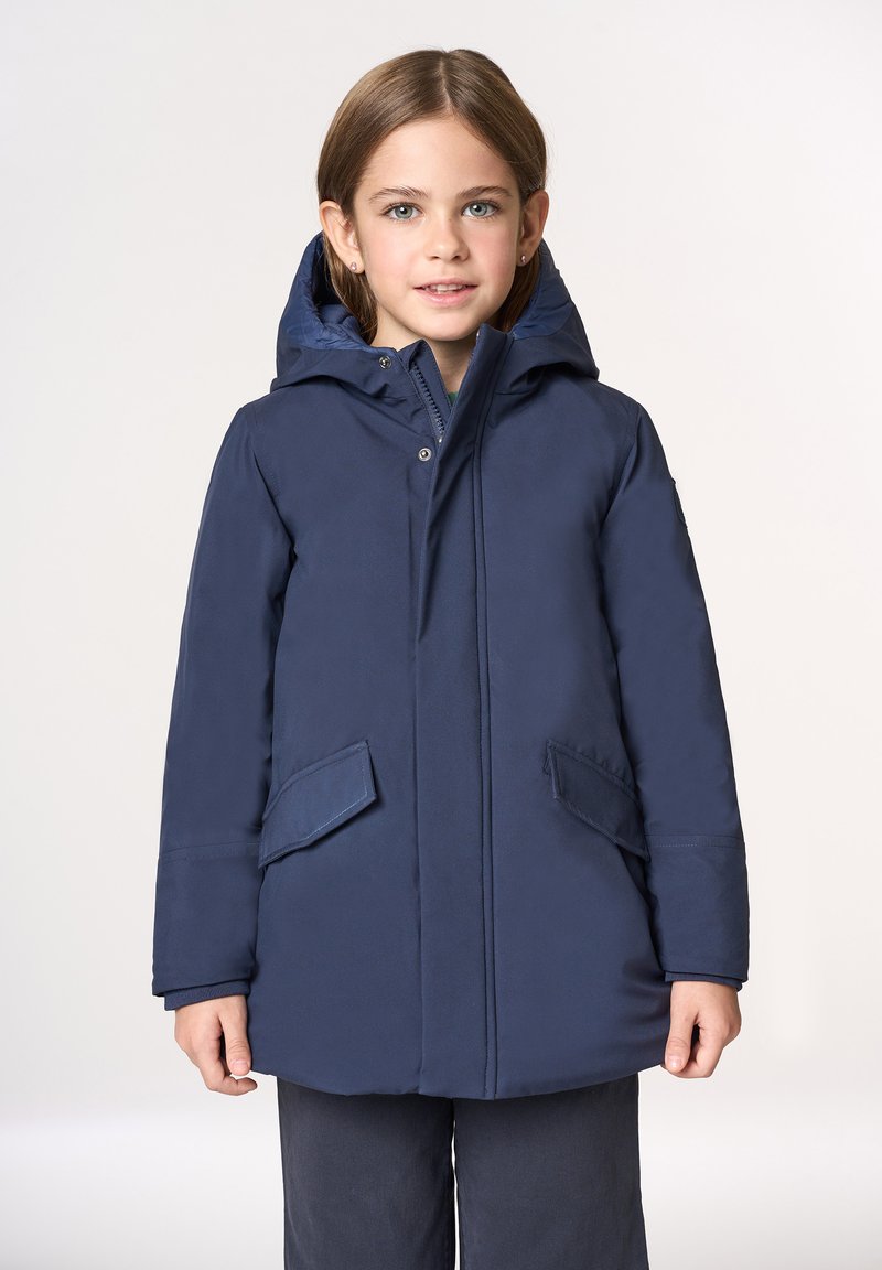 Cappotto imbottito blu scuro con cappuccio, dotato di una cerniera frontale e due grandi tasche applicate. Tessuto liscio con cuciture minimaliste.