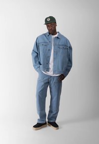 Ανοιχτό μπλε, υπερμεγέθες τζιν μπουφάν με δύο τσέπες στο στήθος, συνδυασμένο με παντελόνι στο ίδιο ανοιχτό μπλε και μαύρα παπούτσια slip-on. Πράσινο καπέλο ολοκληρώνει την εμφάνιση.