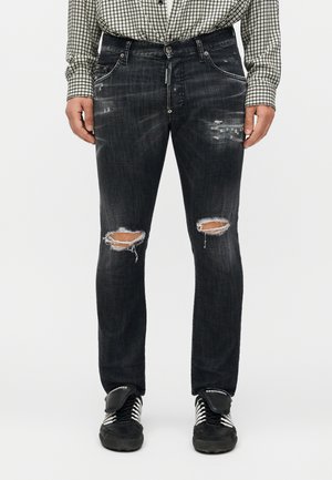 Sorte slidte jeans med revne knæ båret med sorte og hvide sneakers og en sort-hvid ternet skjorte.