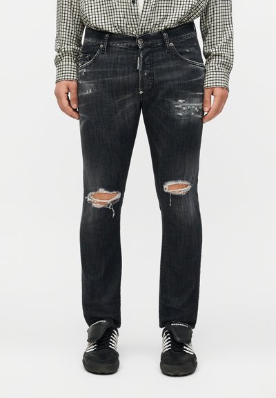 Svarta slitna jeans med trasiga knän, använda med svartvita sneakers och en svartvit rutig skjorta.