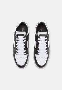 Scarpe da ginnastica in bianco e nero con tomaia in pelle nera testurizzata, lacci bianchi, punta perforata e un piccolo logo di lato.