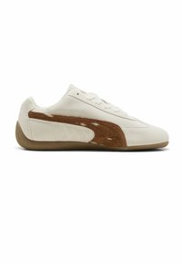 Baskets basses blanches avec une bande texturée marron clair, des lacets blancs et une semelle en caoutchouc colorée, présentées sur un fond blanc.