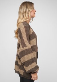 Strikket cardigan med brunt og beige stripemønster, lange ermer og løs passform med ribbestrikkede mansjetter og kant.