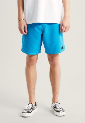 Blaue Badeshorts aus leichtem Material, mit schrägen Seitentaschen, kontrastierenden weißen Nähten und einem kleinen schwarzen Logopatch.