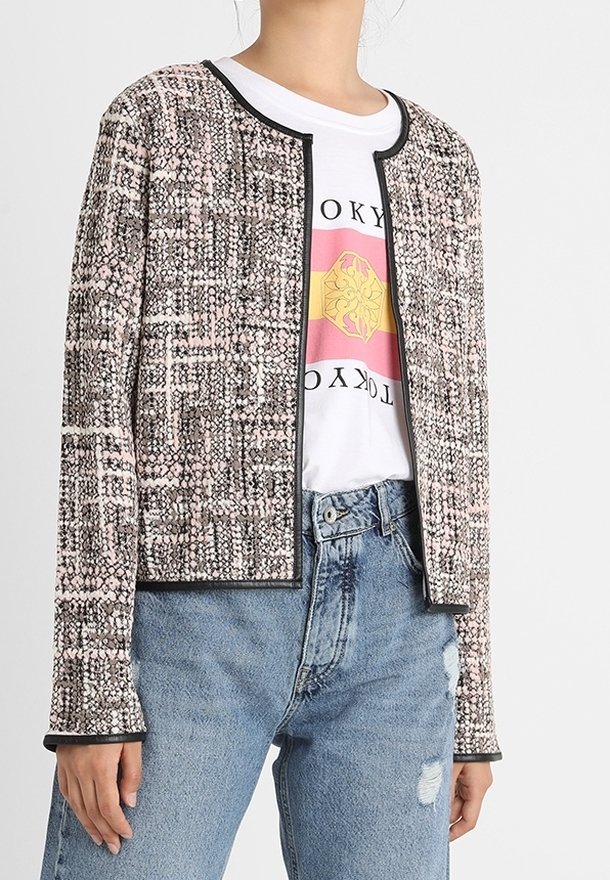 Marynarka w stylu tweed w odcieniach różu i szarości, z okrągłym dekoltem i czarnymi wykończeniami, w zestawieniu z koszulką graficzną i jasnoniebieskimi dżinsami.