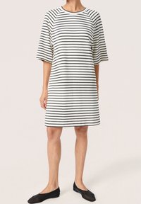 Abito a strisce bianche e nere di lunghezza al ginocchio con scollatura rotonda e maniche corte raglan. Indossato con scarpe basse nere. Tessuto morbido.