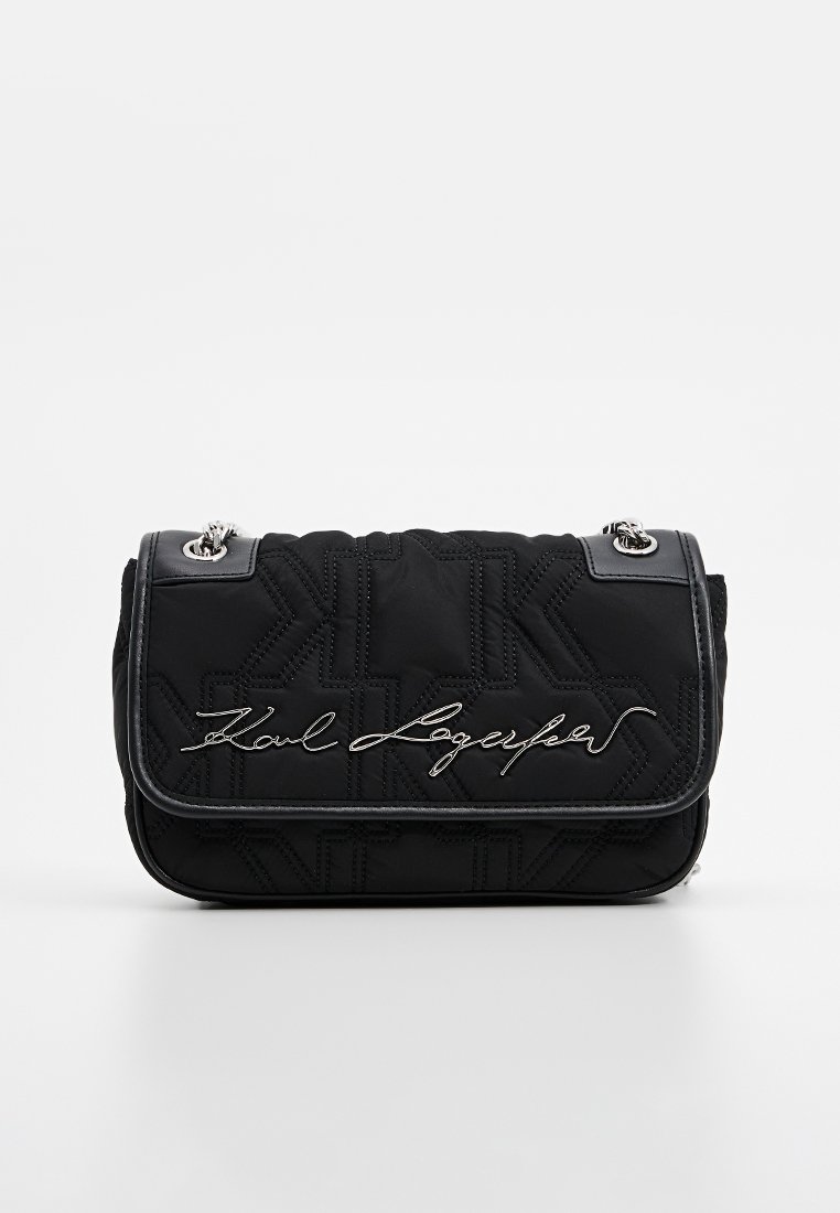 Sac à main noir matelassé avec des accessoires en métal argenté. Présente un rabat à repli et la signature de Karl Lagerfeld en cursive. Motif texturé sur la surface.
