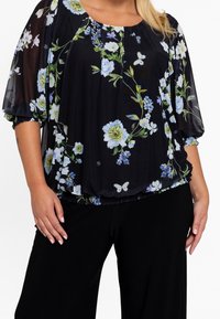 Sort blomsterbluse med korte ærmer, der har blå og grønne blomster og sommerfugle. Blødt, gennemsigtigt stof med en samlet kant.