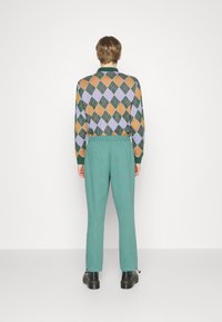 Flerfarget argyle-genser med grønne, oransje og lavendel diamanter; paired med lyseblå bukser; brukt med svarte sko.