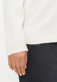 Crèmekleurige gebreide trui met geribbelde manchetten, voorzien van een zachte textuur en een ontspannen pasvorm, gecombineerd met donkere denim.