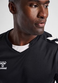 Zwart sportshirt met V-hals en witte accenten, gemaakt van gladde, ademende stof. Logo zichtbaar op de voorkant.