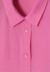 Chemise rose à boutons avec col et deux boutons, fabriquée dans un tissu texturé à finition lisse.