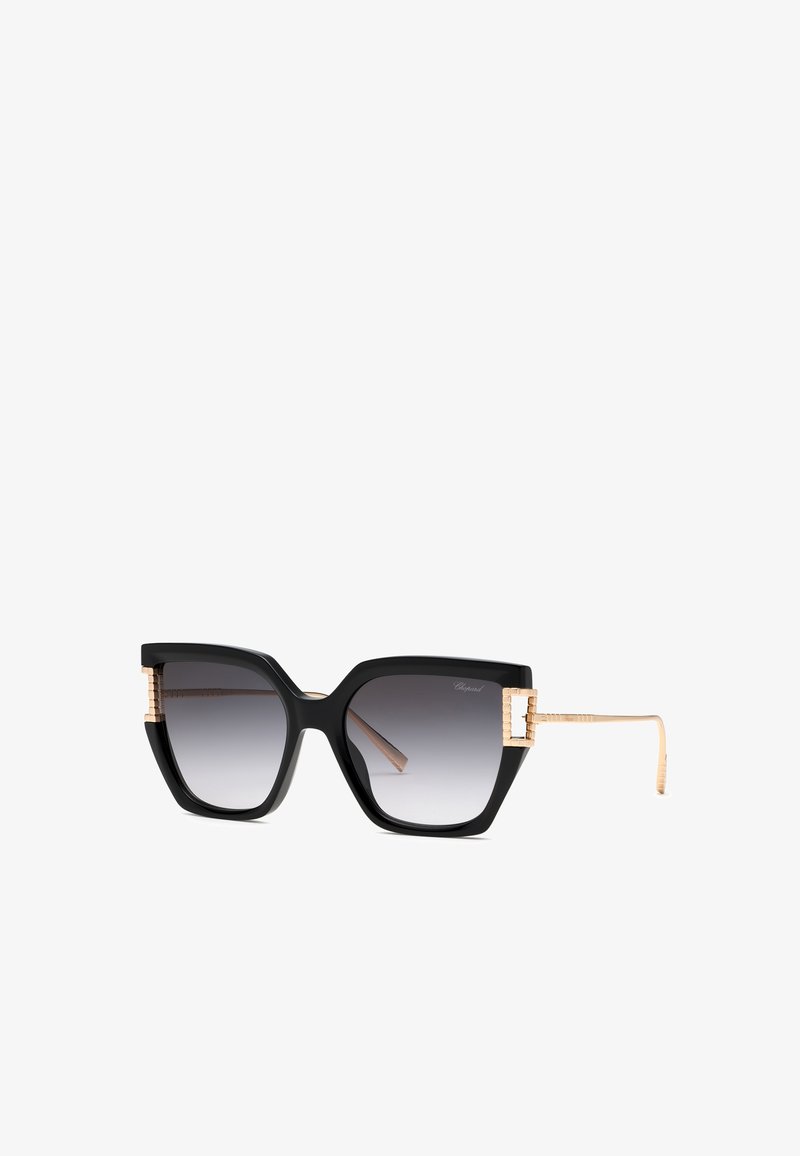 Lunettes de soleil carrées noires oversize avec verres gris dégradés et branches fines en métal doré avec charnières décoratives.