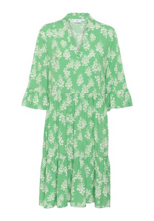 Groene bloemenjurk met een v-hals, uitlopende mouwen en een gelaagd zoom. Heeft witte bloemmotieven op een lichtgroene achtergrond.