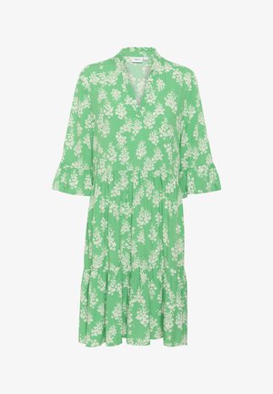 Zelené květinové šaty s výstřihem do V, rozšířenými rukávy a víceúrovňovým lemem. Mají bílé květinové vzory na světlém zeleném pozadí.