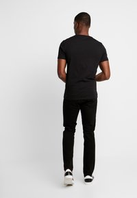 Camiseta de algodón negra de manga corta, combinada con jeans ajustados negros y zapatillas blancas con acentos en negro y gris.