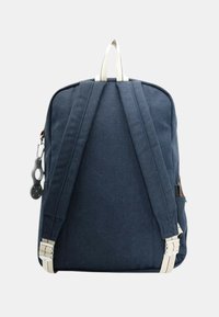 Sac à dos en toile bleu marine avec des poignées crème, deux bretelles à l'arrière et une poche zippée. Il dispose d'une boucle pour des fixations sur le côté.