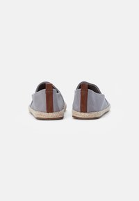Ballerines en toile grise avec des accents en cuir marron et des détails en jute sur la semelle. La vue arrière montre un tissu lisse et un talon structuré.