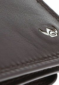 Coin de portefeuille en cuir marron foncé avec des coutures détaillées et un petit emblème argenté en forme de tête d’animal stylisée.