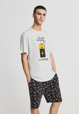 Maglietta grigia in cotone con testo grafico e design a batteria. Pantaloncini neri con motivi a batteria colorati. Abbigliamento casual da casa per il relax.