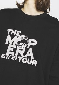 Sudadera negra con cuello redondo que presenta un atrevido texto en blanco: "THE MOP ERA 67/21 TOUR" y un gráfico de un globo en el centro.