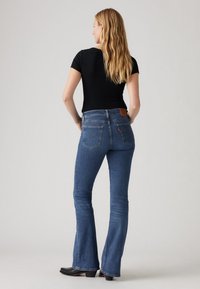 Läikivad sinised kitsad teksapüksid, millel on keskmise kõrgusega vöökoht, kaks tagataskut ja pruun nahast brändiplaaster vöörihmale.