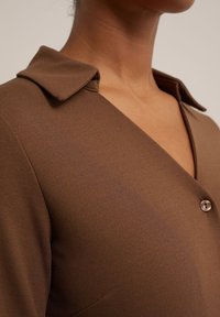 Brun klänning med krage, slät textur och enstaka knappstängning. Närbild som framhäver tyget och halsringningen.