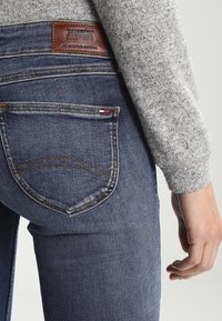 Vaqueros de denim azul oscuro con una etiqueta de cuero, costuras doradas y un solo bolsillo trasero que presenta un pequeño acento de marca.