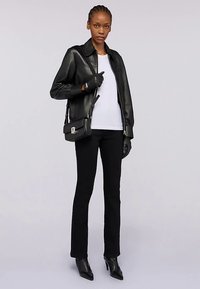 Černá kožená bunda přes bílé tričko, doplněná černými kalhotami a rukavicemi. Oblečení doplňuje malá černá kabelka. Kotníkové boty na podpatku.