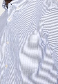 Blå och vit randig skjorta med knapp, försedd med en bröstficka, klassisk krage och texturerad bomullstyg.