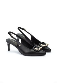Zapatos de tacón en piel negra con tirante en el talón, puntera afilada, detalle de hebilla con acentos dorados y un tacón delgado de altura media. Textura suave y diseño minimalista.