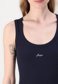 Laivaston sininen ribbede sleeveless-toppi, jossa on pyöreä kaula-aukko. Rinnassa on pieni valkoinen "Boss" -logo. Materiaali näyttää olevan sileä ja joustava.