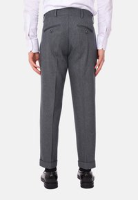 Pantaloni grigi su misura con una texture liscia, orli risvoltati e due tasche posteriori, indossati con scarpe nere.