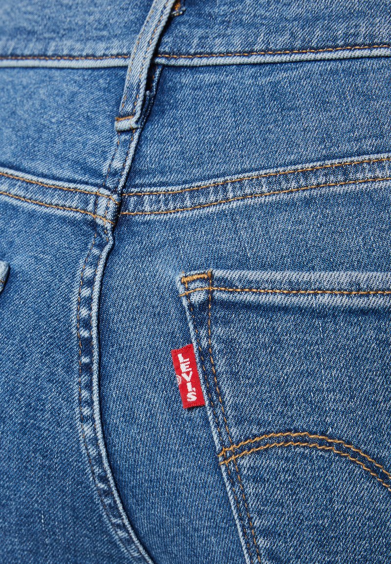 Blaue Denim-Jeans mit orangefarbenen Nähten, die ein rotes "Levi's"-Label an der Gesäßtasche und ein klassisches Fünf-Taschen-Design aufweisen.