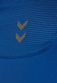 Blå atletisk stof med et struktureret mønster, prydet med to sorte nedadgående chevron-accenter. Glat tekstur med kontrast i materialet.