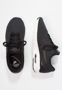 Musta Nike-kengät, joissa on teksturoitu päällinen, valkoinen pohja ja perinteinen nauhoitus. Varressa on ilmapussiyksikkö ja kielelle on painettu logo.