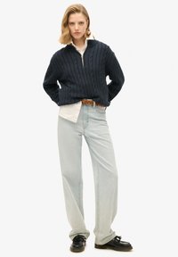 Granatowy sweter z grubym splotem i wysokim kołnierzem, z półzamkiem; noszony na białej koszuli i jasnoniebieskich szerokich dżinsach, zestawiony z czarnymi butami.