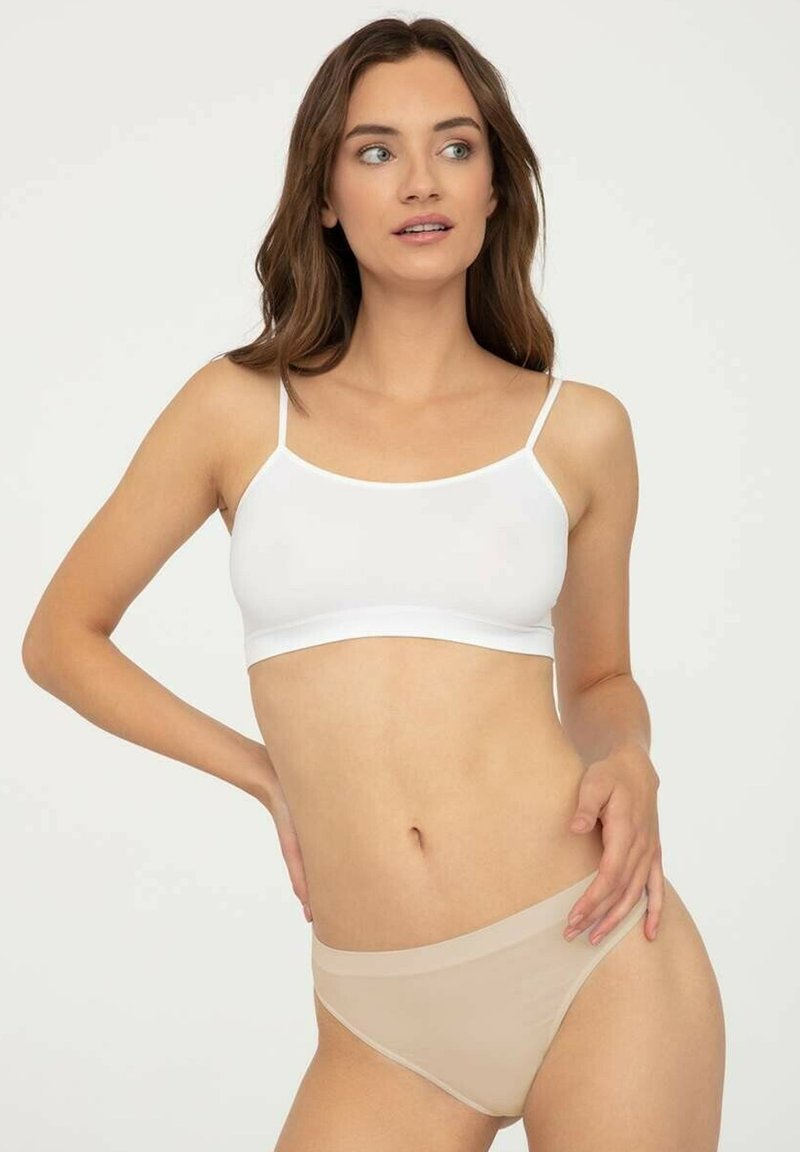 Biała biustonosz braletka z cienkimi ramiączkami, zestawiona z cielistymi bezszwowymi majtkami bikini. Gładki materiał, minimalistyczny design i dopasowany kształt.