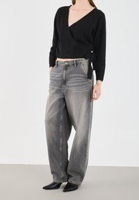 Czarny sweter z długim rękawem, zestawiony z szarymi luźnymi dżinsami o wyblakłym odcieniu, dopełniony czarnymi szpilkami w szpic.