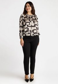 Mustat ja valkoiset kuviolliset paitapuserot, joissa on pitkät hihat, pyöreä kaula-aukko ja elastinen vyötärö, yhdistettyinä mustiin istuviin housuihin ja mustiin korkokenkiin.