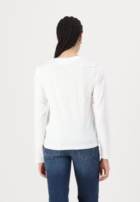 Langærmet hvid skjorte med rund hals, glat tekstur og tætsiddende design. Sammen med blå jeans, der viser et enkelt bagview.
