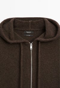 Hnědá kašmírová mikina s hrubým pleteným vzorem, s celoplošným zipem a velkou kapucí. Štítek viditelný uvnitř.