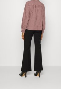 Rot-weiße Karobluse mit Puffärmeln, elastischen Bündchen und einer Passe. Kombiniert mit schwarzen Schlaghosen und schwarzen hohen Schuhen.