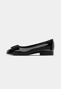 Ballerine in vernice nera con punta arrotondata, caratterizzata da un nodo decorativo sulla parte anteriore e un tacco basso, arrotondato. Superficie liscia e lucida.
