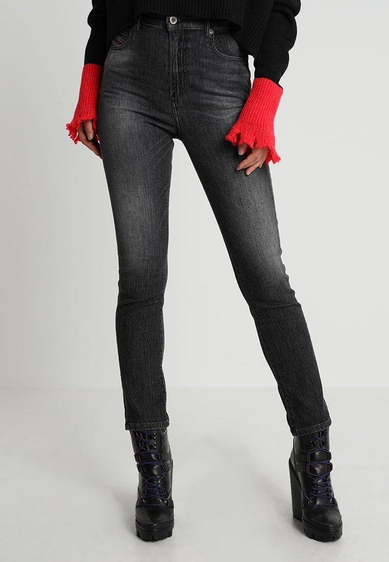 Jean skinny noir à taille haute, en denim. Porté avec un pull noir et des poignets accentués rouges. Associé à des bottines plateformes noires épaisses.