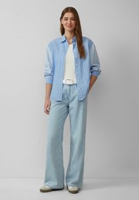 Blau-weiß gestreiftes Hemd mit Knöpfen, weißes Tanktop und hellblaue weite Jeans. Ein weißer Gürtel und beiges Schuhwerk runden das Outfit ab.