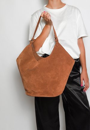 Schokoladenbraune Wildleder-Schultertasche mit einem lässigen Design, verfügt über eine große Öffnung und zwei robuste Griffe, vor einem schlichten Hintergrund.