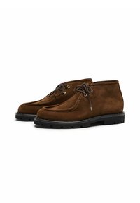 Stivali chukka in suede marrone con punte arrotondate, cuciture a contrasto, occhielli in metallo e suole in gomma nera con tacchetti.